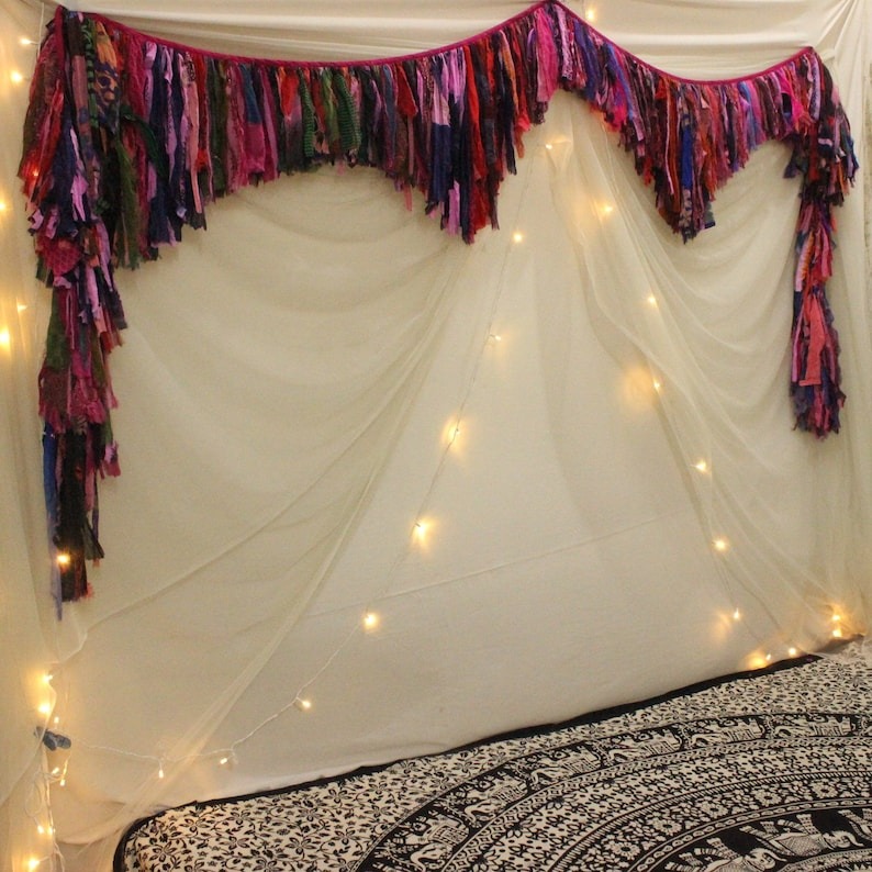 Handmade boho valance made from upcycled fabric strips used as bedroom wall decor with soft white drape and fairy lights